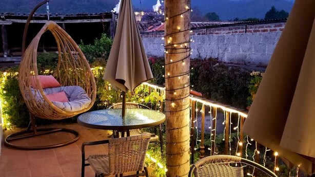 An outdoor patio with wicker furniture, a round table, and string lights. - Luna Maya Antigua Hotel (Antigua Guatemala)