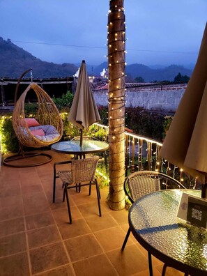 An outdoor patio with wicker furniture, a round table, and string lights. - Luna Maya Antigua Hotel (Antigua Guatemala)