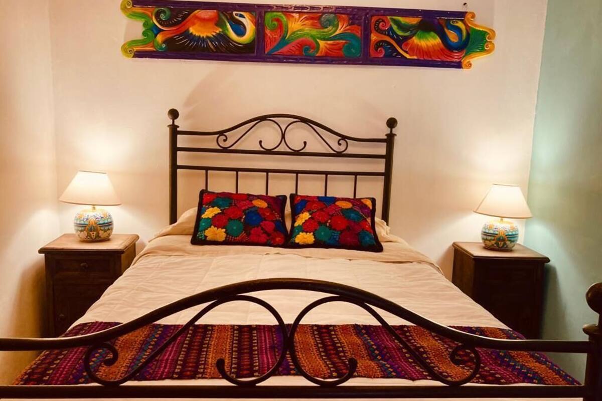 A bed with a black metal frame, two pillows with colorful patterns, and two bedside lamps on wooden nightstands.