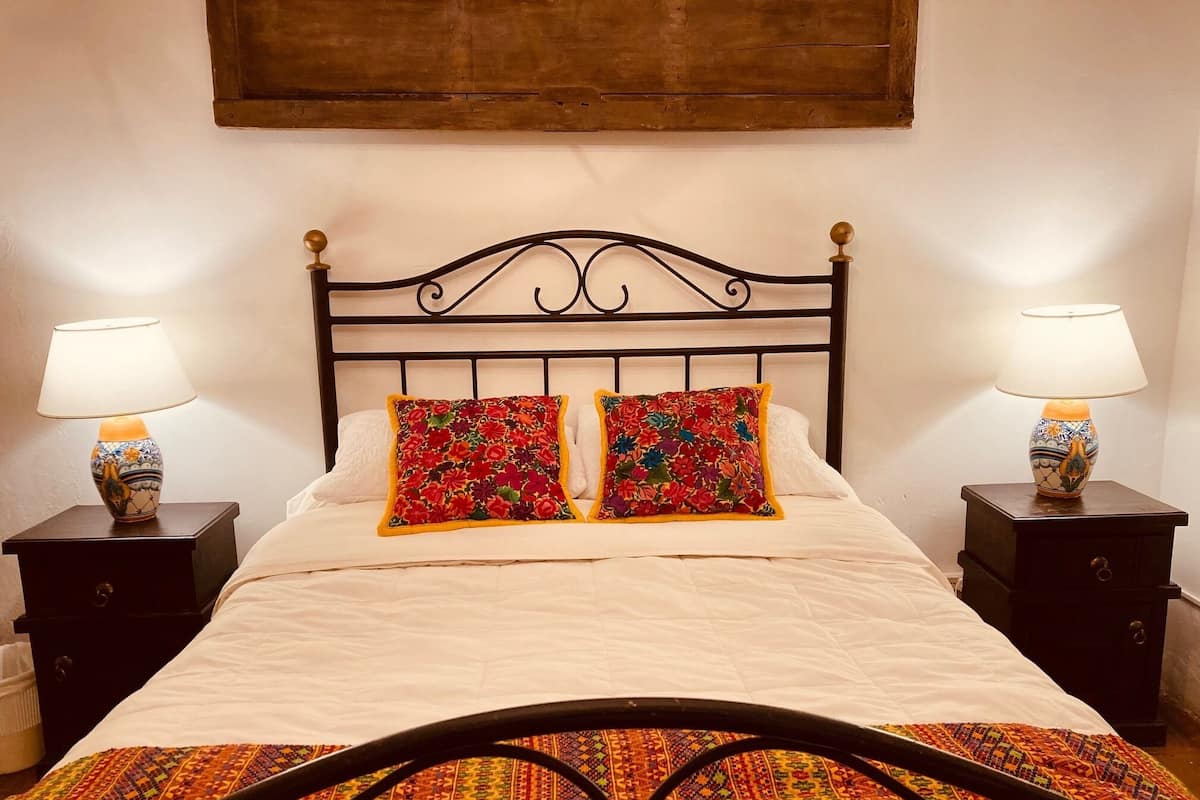 A bed with a white duvet, two decorative pillows, a patterned bedspread, and two bedside tables with lamps.