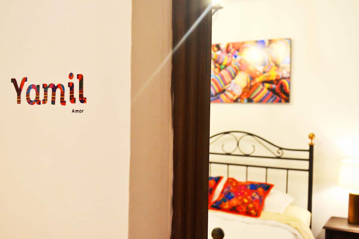 A bedroom with a bed, a nightstand, a lamp, and a colorful painting on the wall.