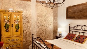 A bedroom with a bed, a wooden wardrobe with floral designs, a chandelier, and a nightstand with a lamp. - Luna Maya Antigua Hotel (Antigua Guatemala)