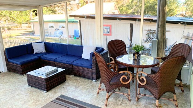 A covered patio area with a blue sectional sofa, wicker chairs, a glass-top table, and a small potted plant. - Off Duty Retreat ~Sleeps 10, Boat Slip, Screen Porch, Lots of Parking, 2 Grills (Steinhatchee)