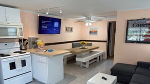 A compact kitchen with a microwave, stove, and a popcorn container. There is a dining area with a table and benches, and a gray sofa in the living area. - Off Duty Retreat ~Sleeps 10, Boat Slip, Screen Porch, Lots of Parking, 2 Grills (Steinhatchee)