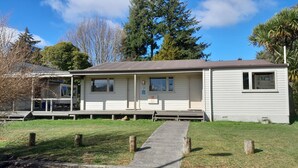 Une maison mobile de plain-pied avec un porche, une petite dépendance attenante et une cour gazonnée.