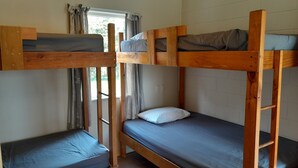 Une chambre avec un lit superposé, une fenêtre, des rideaux et un mur blanc.