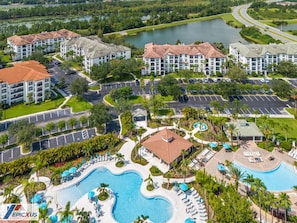 A resort with multiple buildings, a large swimming pool, and a lake in the background.