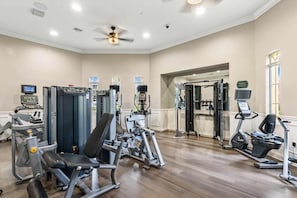 A gym with various exercise machines, a ceiling fan, and a large mirror.