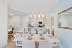 A modern dining area with a white table set for six, a kitchen in the background, and a large mirror on the wall. - The Epic 00106 Vista Cay Resort Orlando Florida (Orlando)
