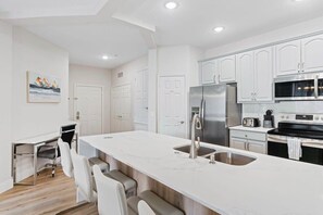 A modern kitchen with white cabinetry, a large island with a sink, and stainless steel appliances.