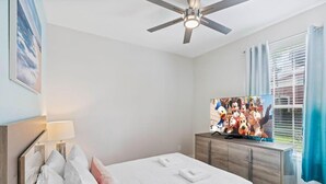 Une chambre à coucher avec un lit, un ventilateur de plafond, une télévision et une fenêtre avec des rideaux.