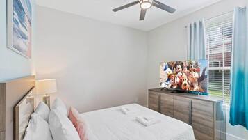 A bedroom with a bed, a ceiling fan, a TV, and a window with curtains.