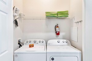 A laundry area with two Whirlpool washers, a fire extinguisher, and a shelf with folded towels. - The Epic 00106 Vista Cay Resort Orlando Florida (Orlando)