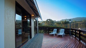 Une terrasse en bois avec deux chaises blanches et un mur en pierre.