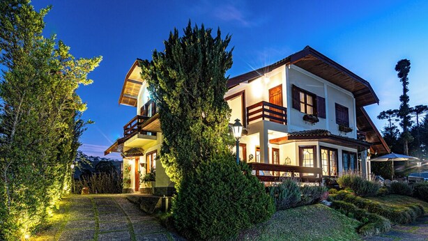 Une maison à deux étages avec un balcon et un jardin bien éclairé au crépuscule.
