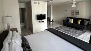 A hotel room with a large bed, a TV mounted on the wall, a sofa, and a ceiling fan. - Heart of Waikiki w/ Kitchen - Free Parking - King Bed - Mountain View (Honolulu)