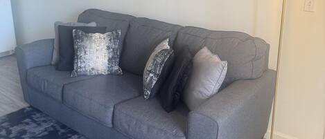 Un canapé gris agrémenté de coussins à motifs, un tapis bleu foncé et deux œuvres d’art abstraites accrochées au mur.