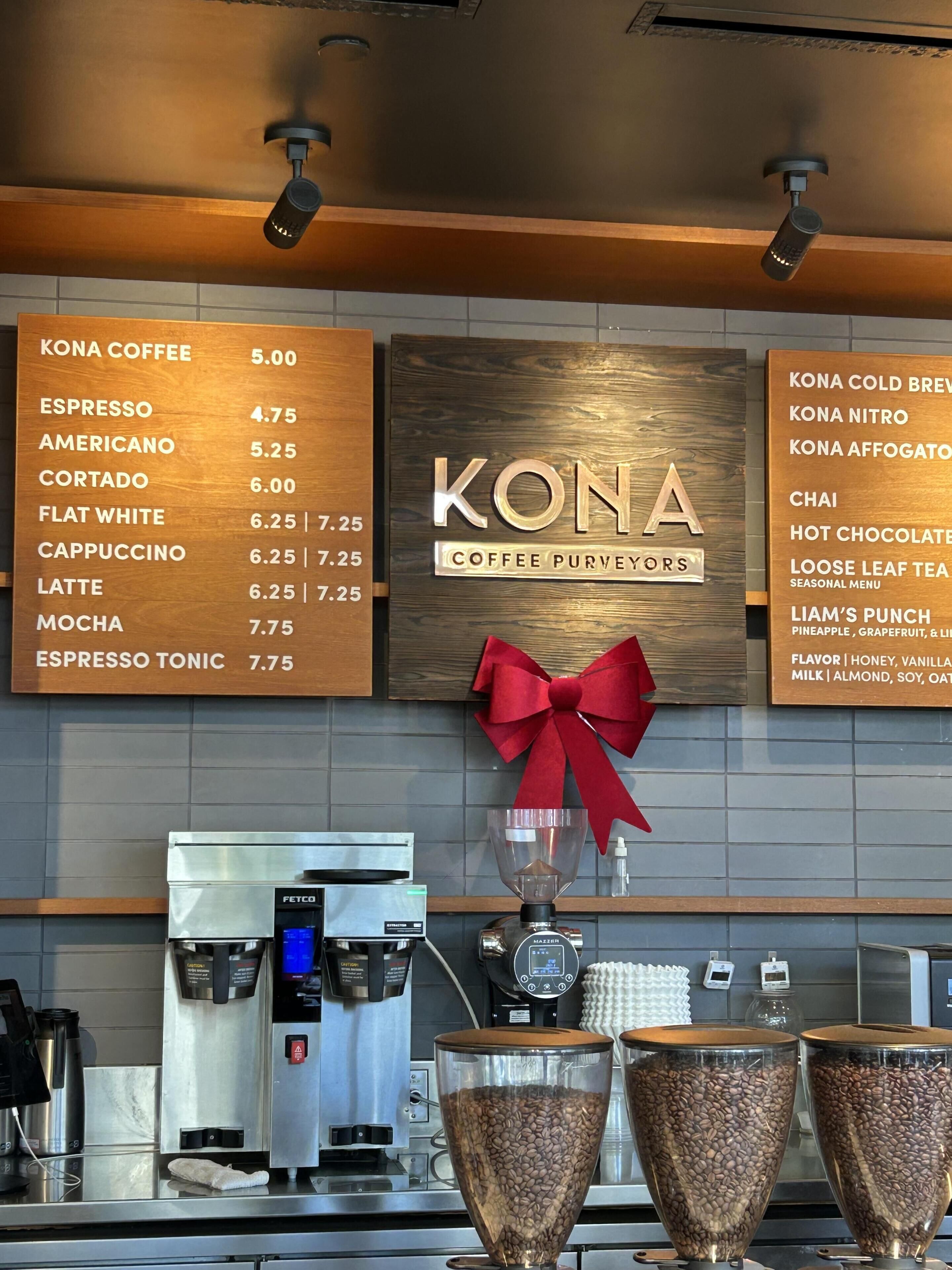 A coffee shop interior with a menu board listing coffee and tea options, a branded sign, and coffee brewing equipment.