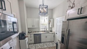 A modern kitchen with stainless steel appliances, white cabinetry, and a patterned backsplash. - Downtown Muskegon Hideaway (Muskegon)