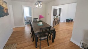 A dining area with a wooden table and chairs, a hanging light fixture, and a potted plant. - Downtown Muskegon Hideaway (Muskegon)