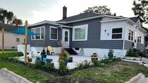 A two-story house with a patio area, outdoor seating, and a garden with a rock border. - Downtown Muskegon Hideaway (Muskegon)