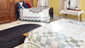 Une chambre avec un mur en briques, une commode en bois, un lit recouvert d’une courtepointe, une table de chevet et une fenêtre avec des rideaux.
