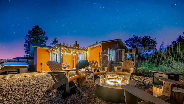 Un'accogliente area esterna con un braciere, sedie in legno e una pergola decorata con luci a stringa.