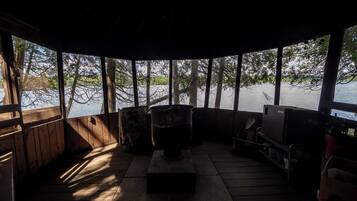 A cabin with a large window overlooking a body of water, a fireplace, and a television.