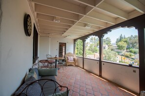 A covered balcony with a table and chairs, a sofa, and a view of a residential area.