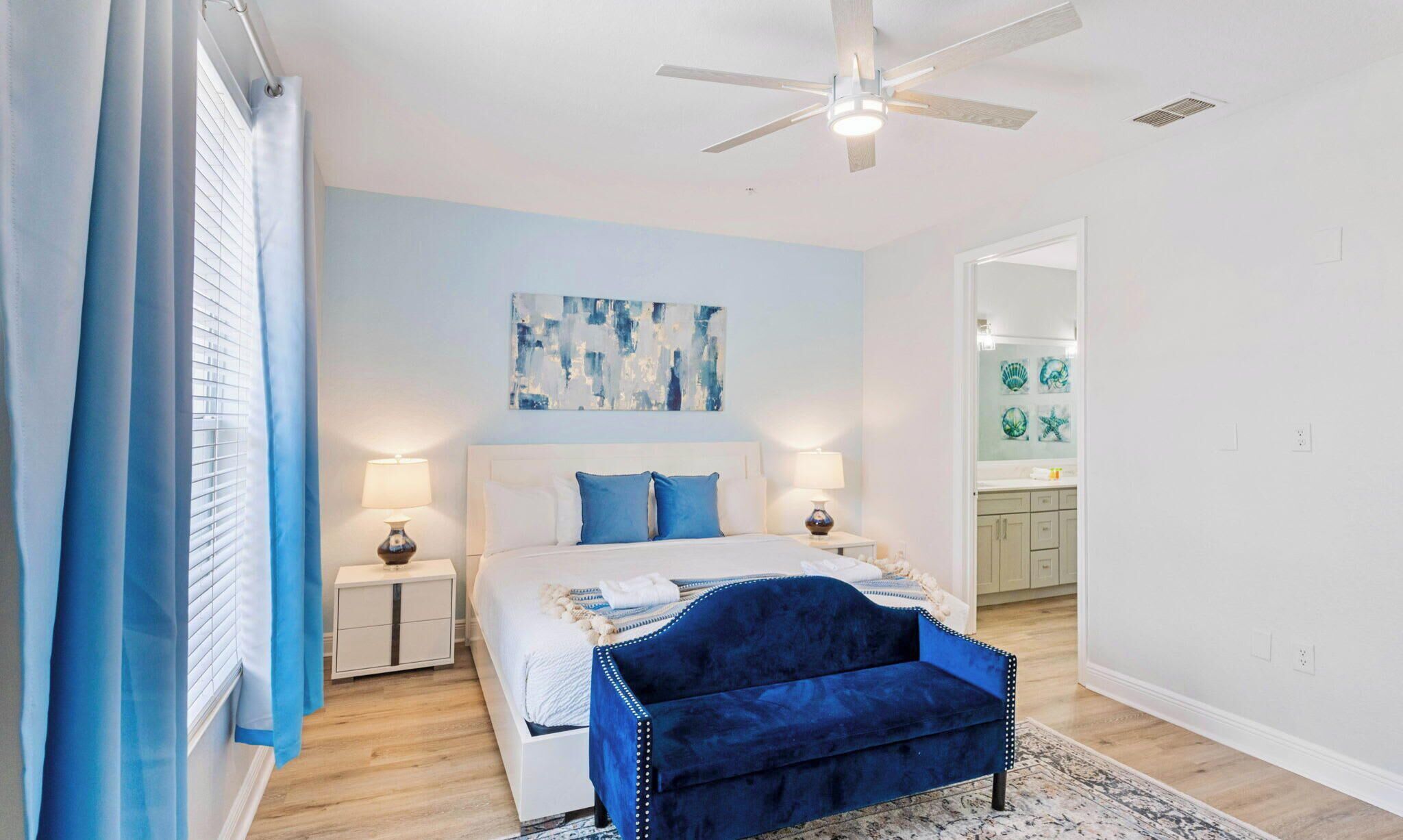 A bedroom with a bed, bedside tables, a ceiling fan, and a blue upholstered bench.