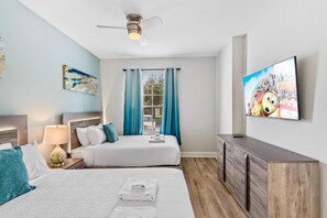 A hotel room with two beds, a ceiling fan, a TV, and a window with curtains.