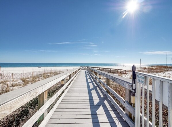 A wooden boardwalk leading to a beach with a clear sky and sun shining. - 5 STARS Beachfront Condo, Indoor/Outdoor Pools, Hot Tub & Tennis! BOOK NOW! (Orange Beach)