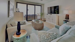 A modern living room with a sofa, armchair, coffee table, and a TV. - 5 STARS Beachfront Condo, Indoor/Outdoor Pools, Hot Tub & Tennis! BOOK NOW! (Orange Beach)
