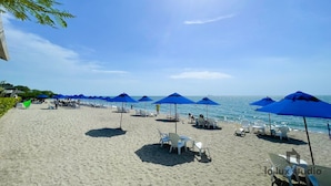A beach with white lounge chairs and blue umbrellas under a clear sky.