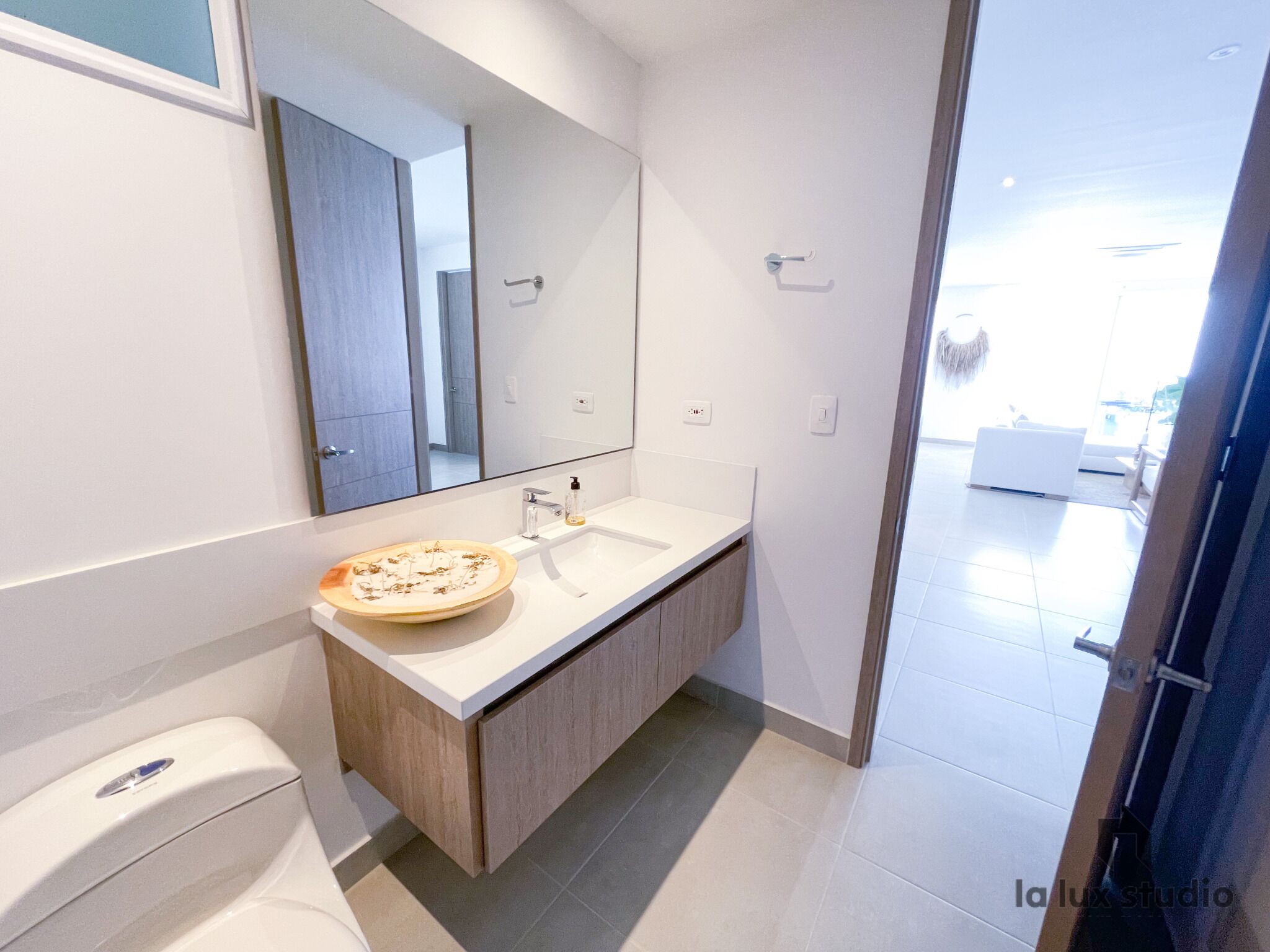 A modern bathroom with a white sink, wooden vanity, and a large mirror.