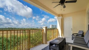 A balcony with a ceiling fan, a view of the cityscape, and a seating area with a patterned rug.