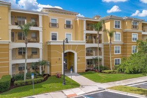 A multi-story residential building with balconies, a central entrance, and a well-maintained lawn.