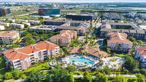 A hotel with a central swimming pool, multiple buildings, and surrounding greenery.