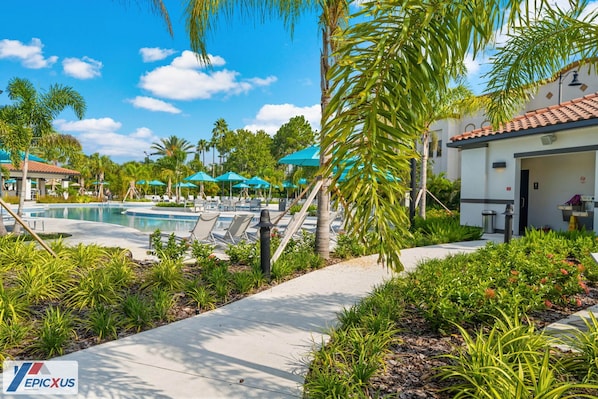 A pool area with lounge chairs and umbrellas, surrounded by palm trees and greenery.