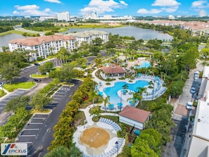 Un resort con una amplia piscina, cancha de tenis y una zona ajardinada con palmeras.