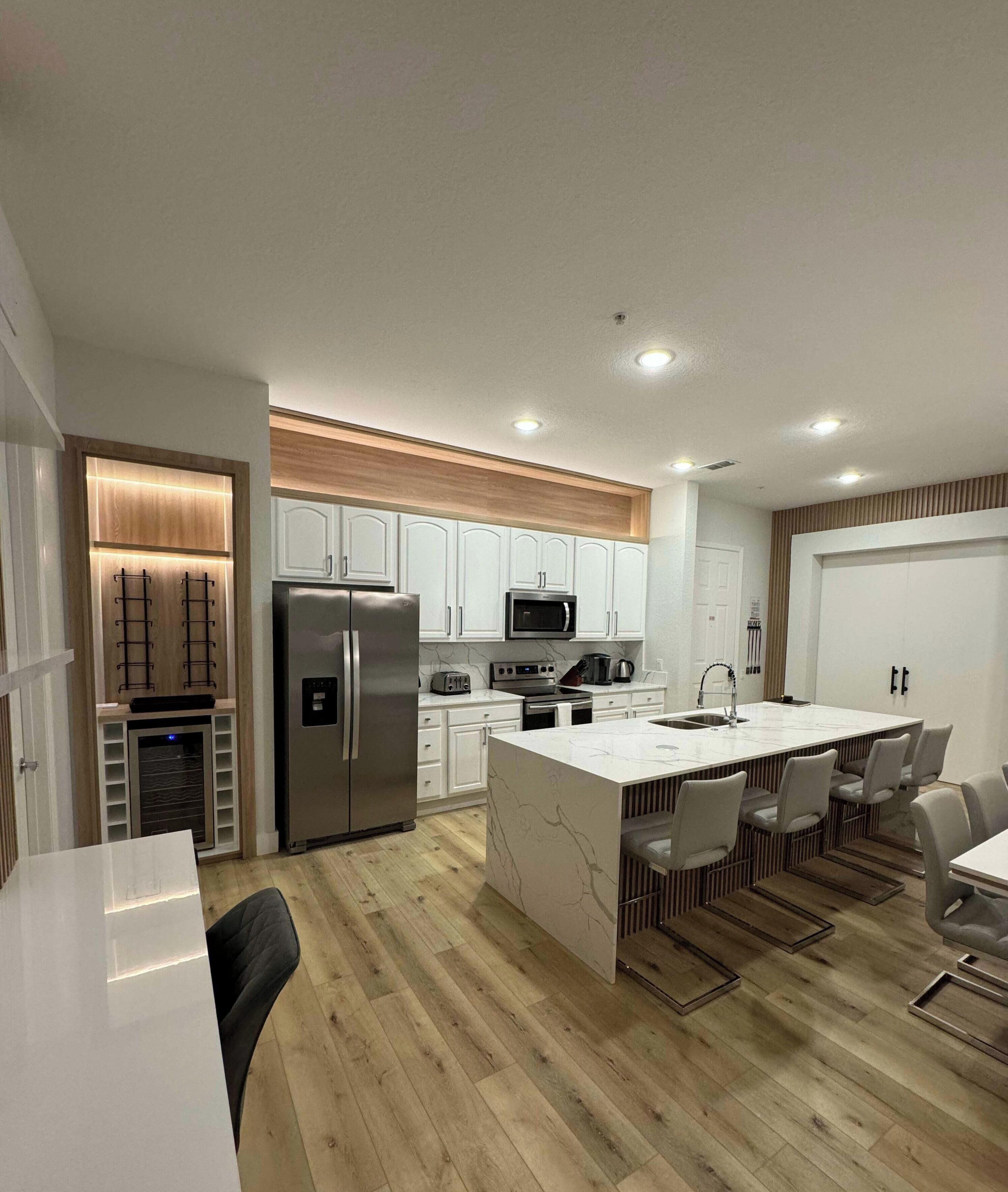 A modern kitchen with white cabinetry, a stainless steel refrigerator, and a central island with seating.