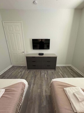 A bedroom with two beds, a TV on a dresser, and a door.