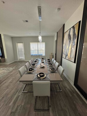 A modern dining room with a long table set for six, flanked by chairs, a chandelier, and artwork on the walls.
