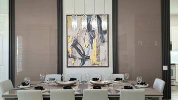 A modern dining room with a long table, white chairs, and a large abstract painting on the wall.