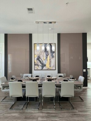 A modern dining room with a long table, white chairs, and a large abstract painting on the wall. - The Epic 24407 Penthouse Vista Cay Resort Orlando FL (Orlando)