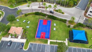 An aerial view of a parking lot with a basketball court, a covered area, and a building with a red roof.