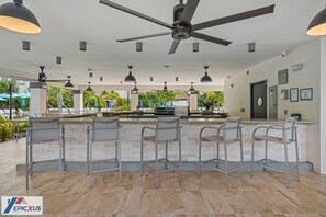Eine Bar mit fünf Metallhocker, einem Deckenventilator und Pendelleuchten.