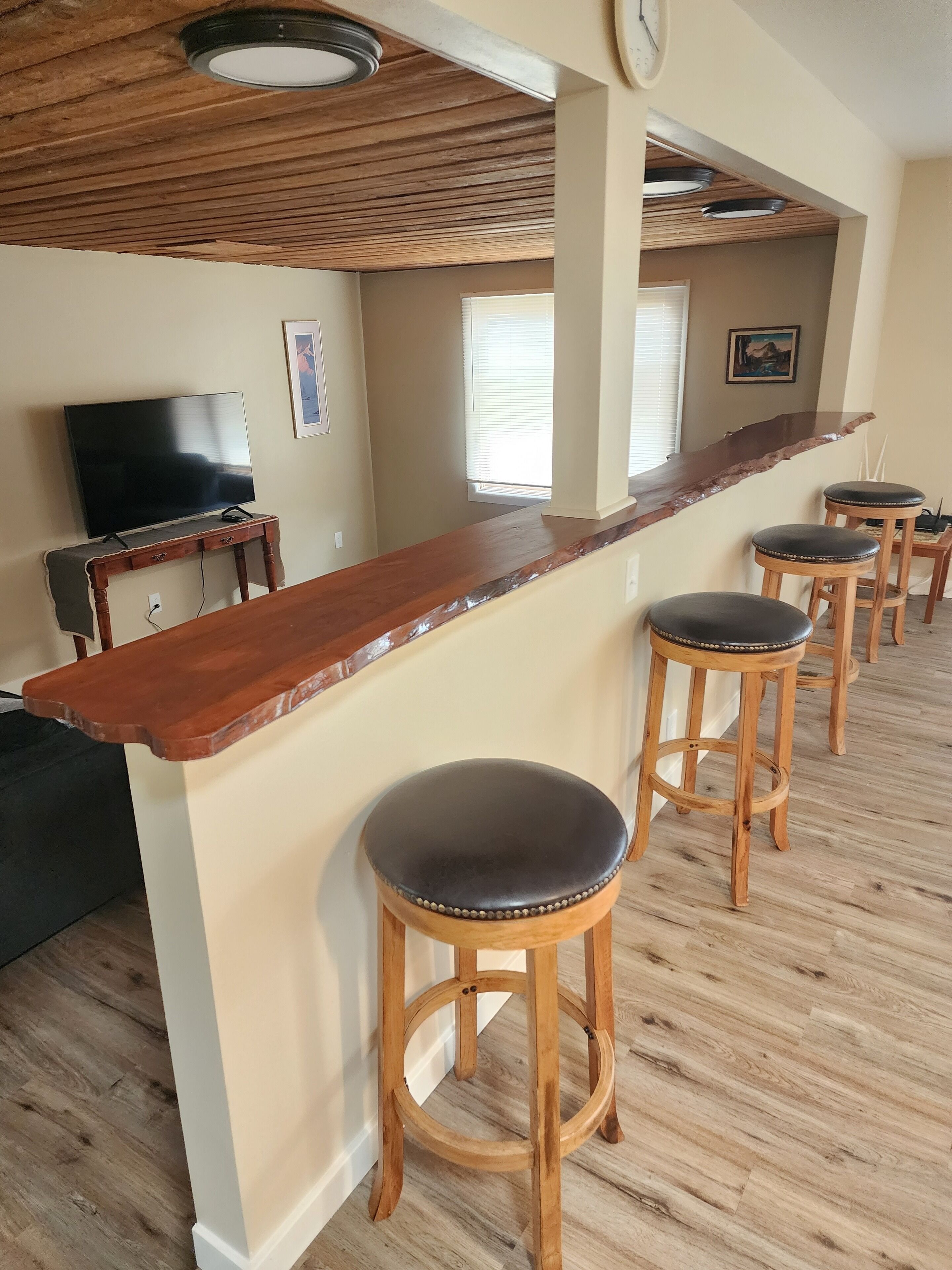 A kitchen with a wooden countertop, bar stools, a TV, and a clock on the wall.