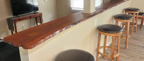 A kitchen with a wooden countertop, bar stools, a TV, and a clock on the wall.