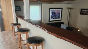 A bar area with wooden stools, a wooden counter, and a ceiling with recessed lighting.